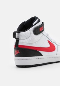 Sapatilhas Nike de cano alto com um cabedal sintético branco e detalhes em preto e vermelho, língua texturizada e uma tira de Velcro para um ajuste seguro.