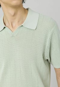Polo-shirt tricoté vert clair avec un motif texturé, un design en V et des manches courtes avec un col côtelé.