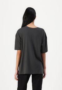 Tmavě šedé oversized tričko vyrobené z měkké látky, s kulatým výstřihem a krátkými rukávy, jednoduchý design bez viditelných vzorů nebo akcentů.