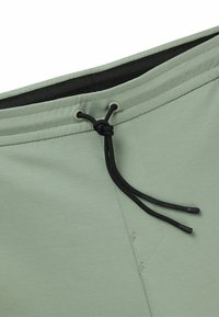 Lichtgroene shorts van gladde stof, met een zwarte trekkoord in de taille en subtiele stikseldetails.