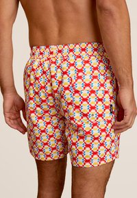Zwemshorts van lichtgewicht stof, met een felrode basis en een geometrisch patroon van gele, blauwe en witte vormen. Elastische tailleband.