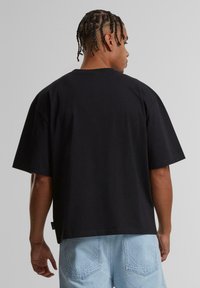 Black short-sleeve t-shirt with a relaxed fit, featuring a crew neckline and a straight hem, worn with light blue denim shorts.