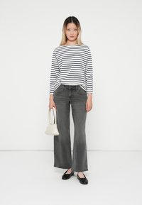 Top a maniche lunghe a righe in bianco e blu navy, abbinato a jeans grigi a vita alta e a gamba larga. Accessoriato con una piccola borsa bianca e ballerine nere.