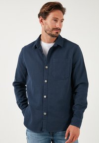 Camicia button-up blu navy realizzata in tessuto testurizzato, dotata di taschino sul petto e bottoni in argento, con maniche lunghe e colletto.