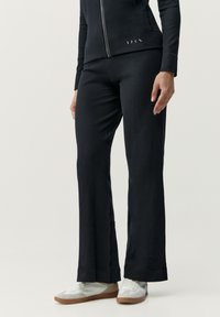 Svarta, åtsittande träningsbyxor med en lätt utsvängning vid ankeln, tillverkade av mjukt material. Kombinerade med ljusa sneakers.