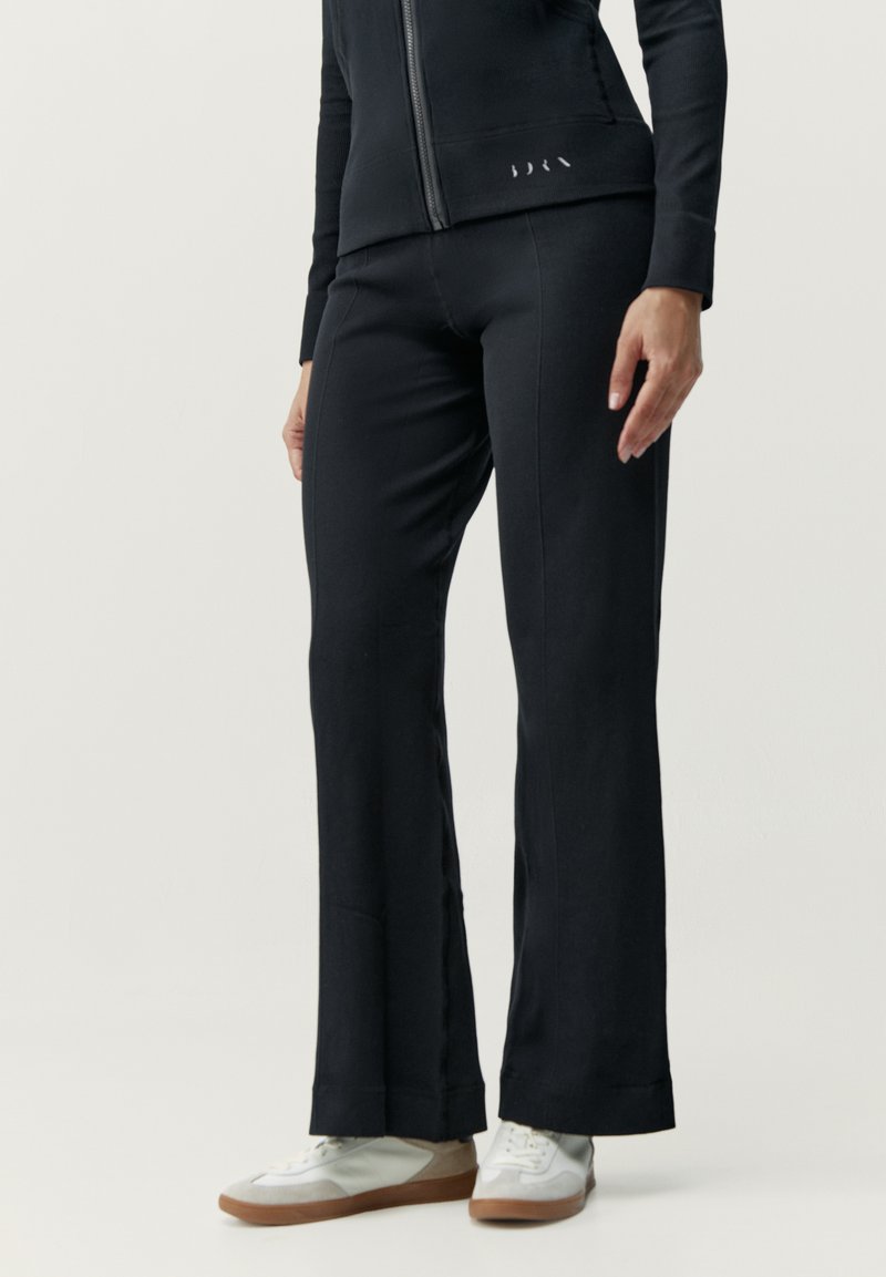 Svarta, åtsittande träningsbyxor med en lätt utsvängning vid ankeln, tillverkade av mjukt material. Kombinerade med ljusa sneakers.