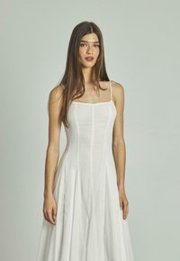 Weißes Leinenkleid mit tailliertem Oberteil und weiter, plissierter Rock. Verfügt über dünne Träger und einen runden Ausschnitt, der eine glatte Textur zeigt.