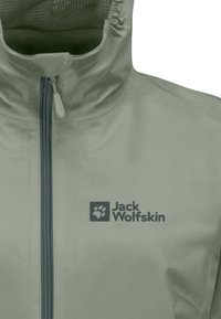 Jasnozielona kurtka zapinana na zamek z wysokim kołnierzem. Posiada ciemne logo na lewej piersi oraz gładką, wodoodporną fakturę materiału.