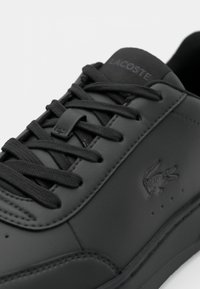 Črne usnjene teniske s okroglo konico, ravnimi črnimi vezalkami, odtisnjenim logotipom na strani in teksturiranimi detajli ob podplatu.