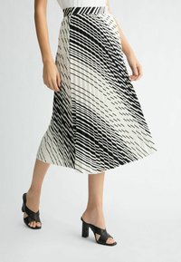 Falda plisada en blanco y negro con rayas diagonales, que cuenta con una cintura alta y un diseño fluido. Combinada con sandalias de tacón negro.