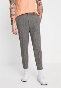 Grå rutig byxor med smal passform, med en midje av medelhöjd och sidofickor, tillsammans med vita sneakers. Slät tygstruktur.