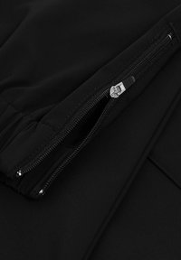 Black fabric with a smooth texture, featuring a zipper detail. The design includes a hidden zip pocket along the seam for functionality.