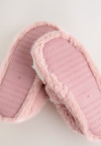 Chaussons roses duveteux avec une surface extérieure en fourrure douce et des semelles en caoutchouc texturées. L'intérieur est doté d'une doublure moelleuse pour le confort. Taille moyenne indiquée.