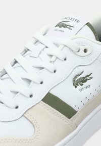 Λευκό δερμάτινο αθλητικό παπούτσι με πράσινες λεπτομέρειες από σουέντ, με υφή στην πλευρική επιφάνεια, λευκά κορδόνια και λογότυπο κροκόδειλου με την επιγραφή "EST. 1933."