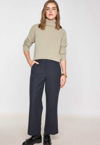 Un pull à col roulé beige clair avec une texture côtelée, associé à un pantalon à taille haute et jambes larges de couleur gris foncé. Des chaussures noires avec des accents décoratifs.