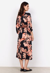 Blumenmaxikleid mit schwarzem Hintergrund, versehen mit großen Pfirsich- und Beigetönen. Lockere Passform, taillierter Schnitt und Dreiviertelärmel.