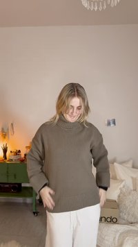 Khaki ribstrikket rullekrave, afslappet pasform og sænkede skuldre, kombineret med hvide bukser, vist i et blødt oplyst rum.