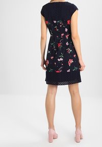 Abito floreale navy con maniche a cappuccio e rifinitura in pizzo. Caratterizzato da motivi floreali nei toni del rosso e del rosa, retro texture, e vita aderente.