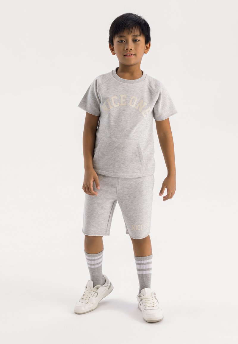 Ungdom grå bomulds t-shirt med "NICE ONE" print, parret med matchende shorts. Hvide sneakers og grå stribede sokker fuldender det afslappede outfit.