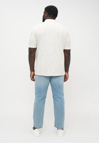 Camicia a maniche corte, di un beige chiaro con un delicato motivo a foglie, abbinata a jeans dritti azzurri e sneakers bianche.