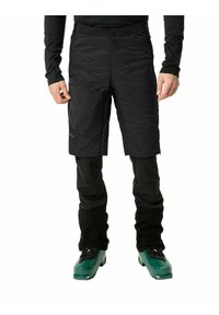 Pantaloni corti neri isolati con superficie texturizzata, abbinati a pantaloni neri aderenti. Gli stivali da sci verdi completano l'outfit.