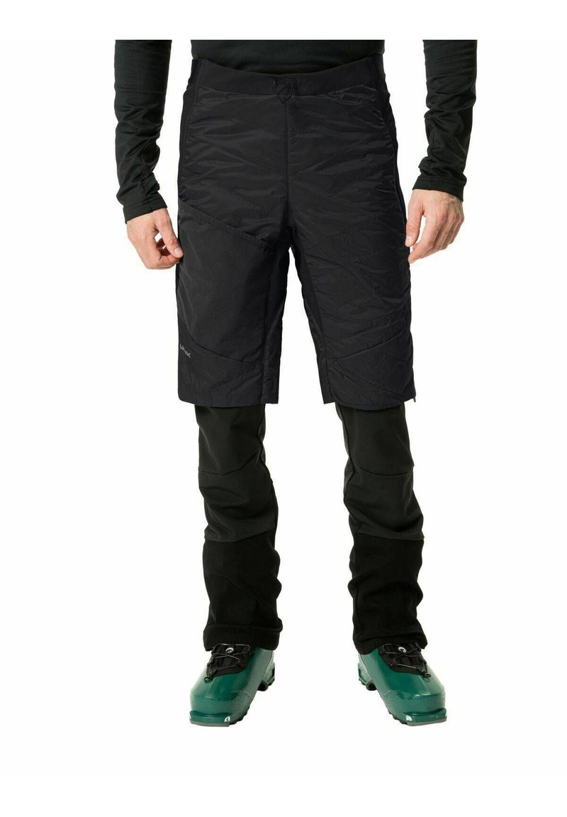 Pantaloni corti neri isolati con superficie texturizzata, abbinati a pantaloni neri aderenti. Gli stivali da sci verdi completano l'outfit.