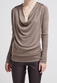 Bruine gedrapeerde trui met lange mouwen, geribbelde zoom en schouderdetails. Zachte textuur met een relaxte pasvorm, gecombineerd met donkere leren broeken.