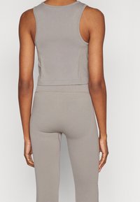 Šedý crop top s přiléhavým střihem, vyrobený z hladké látky. Má široké průramky a zaoblený výstřih, doplněný o odpovídající legíny.