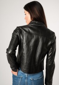 Zwarte leren jack met een getailleerd silhouet, een notched collar en subtiele stiksels. Dracht over denim jeans, waarmee een gladde textuur wordt getoond.