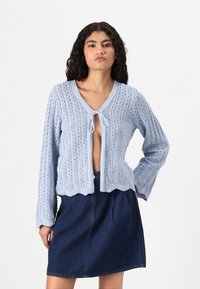 Cardigan lavorato a maglia azzurro chiaro con chiusura a nodo, apertura frontale, colletto a coste e maniche lunghe. Presenta un motivo testurizzato e un orlo a scallop.