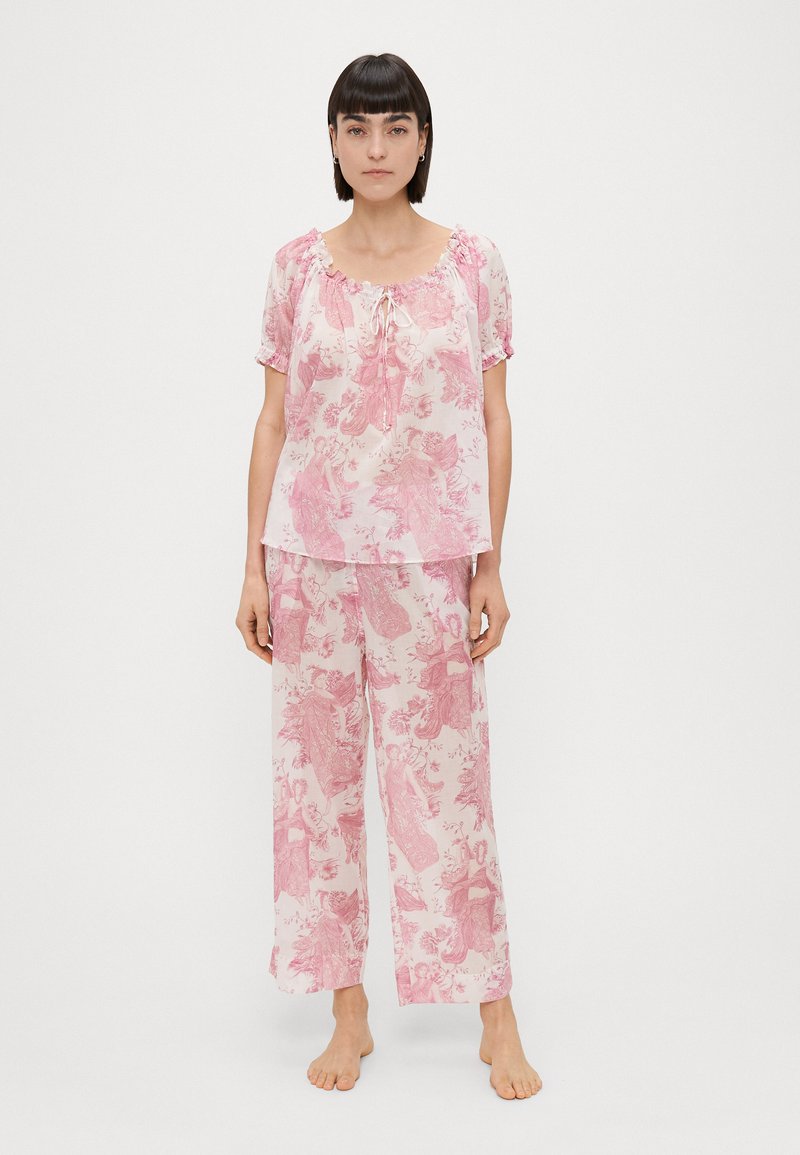 Conjunto de pijama com padrão floral em rosa, apresentando uma blusa leve e fluida com mangas curtas e decote com cordão, emparelhado com calças de perna larga.