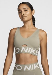 Sports-bh i lys olivengrønn, laget av glatt stoff. Har scoop-hals og nøkkelhull detalj, samt bredt bånd med "PRO NIKE" tekst.