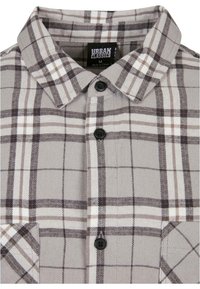 Grijze geruite flanellen shirt met een button-down kraag, zwarte knopen en contrasterende witte en bruine ruitpatronen.