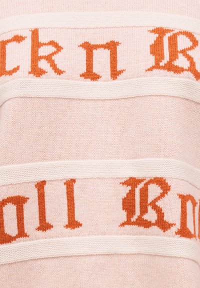 Απαλό ροζ πλεκτό ύφασμα με οριζόντιες κρεμ ρίγες και πορτοκαλί γοτθικό κείμενο που διακρίνεται εν μέρει κατά μήκος των ριγών.