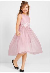 Robe sans manches rose avec broderie florale à la taille, jupe en tulle superposée et ballerines noires avec des accents nœud.