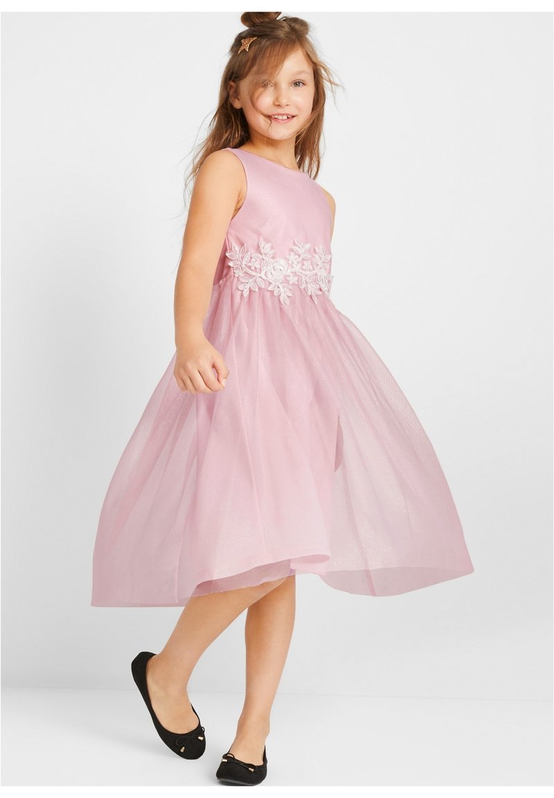 Robe sans manches rose avec broderie florale à la taille, jupe en tulle superposée et ballerines noires avec des accents nœud.