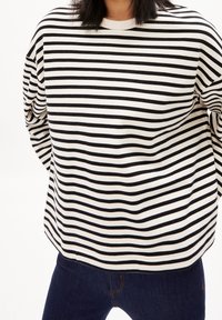 Schwarz-weißer gestreifter Langarmshirt mit rundem Halsausschnitt, lockerer Passform und weicher Textur. Getragen mit dunklen Jeans.