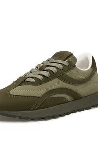 Zapatilla deportiva verde oliva que combina ante y tela, con punta redondeada, diseño de lazada texturizado y suela de goma gruesa.