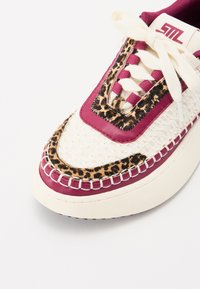 Sneaker mit einem weißen gewebten Textil und burgunderfarbenen Lederakzenten, Leopardenmuster-Detail, strukturiertem Sohlenprofil und cremefarbenen Ösen.