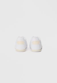 White sneakers with a smooth leather upper, mesh accents, and a beige heel tab. Features round laces and a textured outsole design.