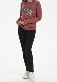 Weinrotes Langarm-Sweatshirt mit grafischem Druck von Vögeln, kombiniert mit schwarzen Skinny Jeans und weißen Sneakers. Weiches Material, lässiger Schnitt.