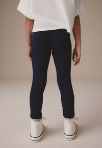 Tumesinised retuusid koos valge, üle suurusega särgiga. Laps kannab valgeid kõrge säärega tossusid mustade detailidega, esitades igapäevast riietust.