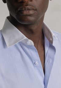 Camisa a rayas azul y blanca con un collar blanco, que cuenta con cierres de botones y una textura suave, mostrando un diseño clásico de camisa.