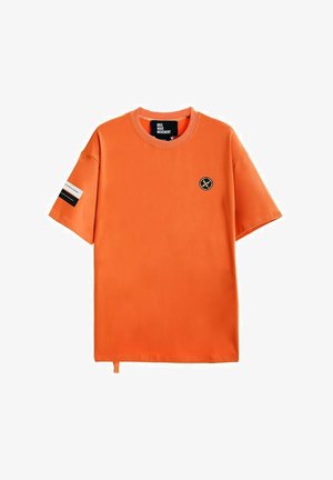 Camiseta de manga corta naranja hecha de una tela suave, con cuello redondo, pequeño logotipo en el pecho y una etiqueta en contraste en la manga.