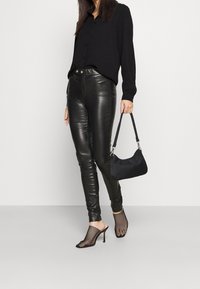 Camicia nera a bottone, pantaloni di pelle nera aderenti, mule con tacco in rete nera e una piccola borsa a tracolla in tessuto nero. Elementi di design semplici e eleganti.