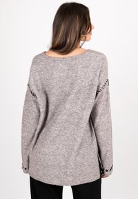 Helles graues Strickpullover mit lockerer Passform, der schwarze Stickakzente an den Ärmeln und einen weiten Ausschnitt aufweist. Weiches, strukturiertes Material.