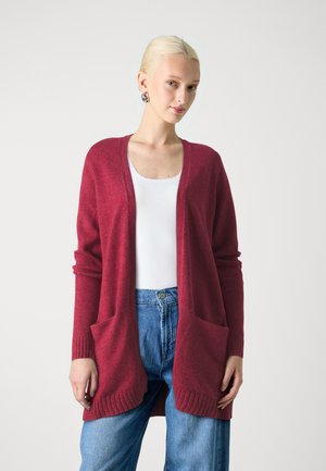 Langer, offener Cardigan in Dunkelrot aus gestricktem Stoff. Mit gerippten Bündchen und zwei vorderen Taschen. Schlichte, weiche Textur, getragen über einem weißen Oberteil.