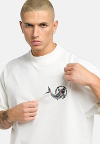 Witte oversized sweatshirt met een kleurrijke visgrafiek op de borst, met raglanmouwen en een zachte, textuurstof.