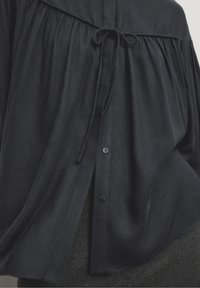 Marineblauwe blouse van lichtgewicht stof, met gatheringdetails op de schouders, een striksluiting en een knoopsluiting langs de voorkant.