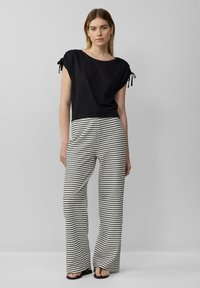 Zwart T-shirt met korte mouwen en geknoopte schouderbanden, gecombineerd met wijd uitlopende broek met een zwart-wit gestreept patroon. Getextureerde stof.